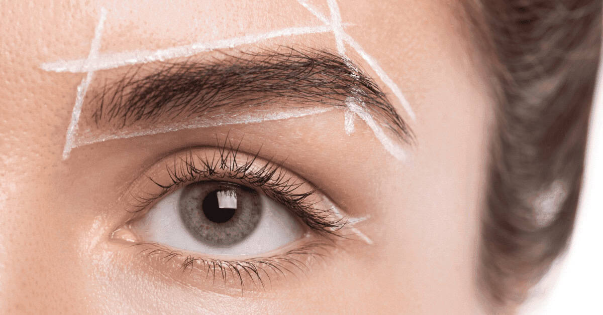 Vast, natural gray eye with detailed eyelashes and shaped eyebrows, white markings on skin indicating eyelash and eyebrow shaping or beauty routine, close-up beauty makeup shot.