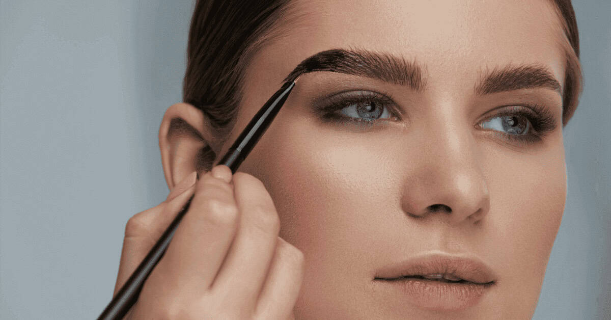 EYEBROW PENCIL SUGGESTIONS FOR A NATURAL LOOK Soft close-up of a woman applying eyebrow makeup with an angled brush, emphasizing flawless beauty and perfectly shaped eyebrows, ideal for eye makeup and enhancing natural eye features.