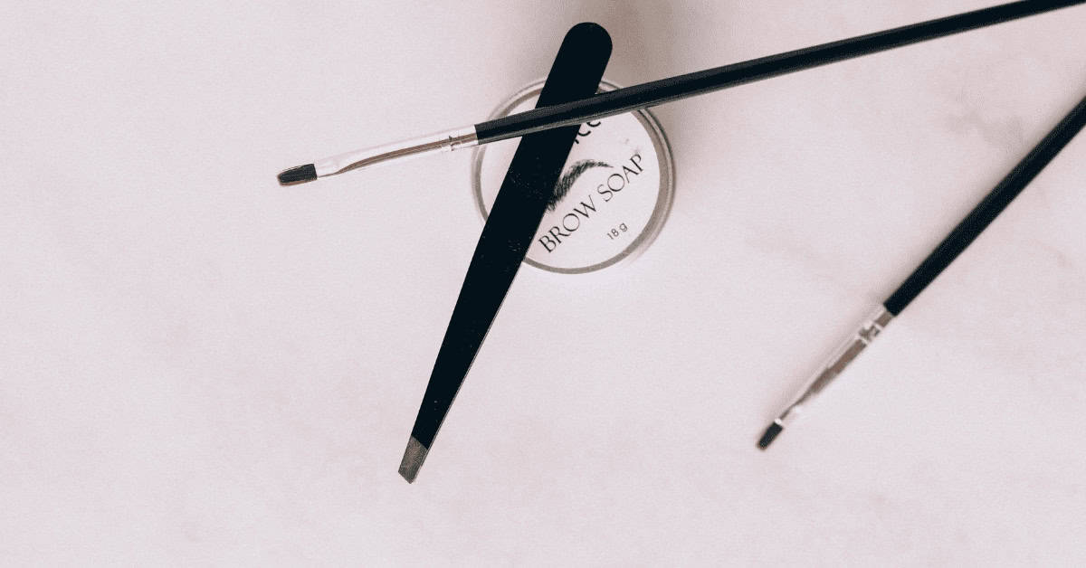 Luxurious black mascara wand with eyelash brush, placed on a white background with a brow soap container, emphasizing eye makeup and beauty tools for enhancing eyelashes and brows.