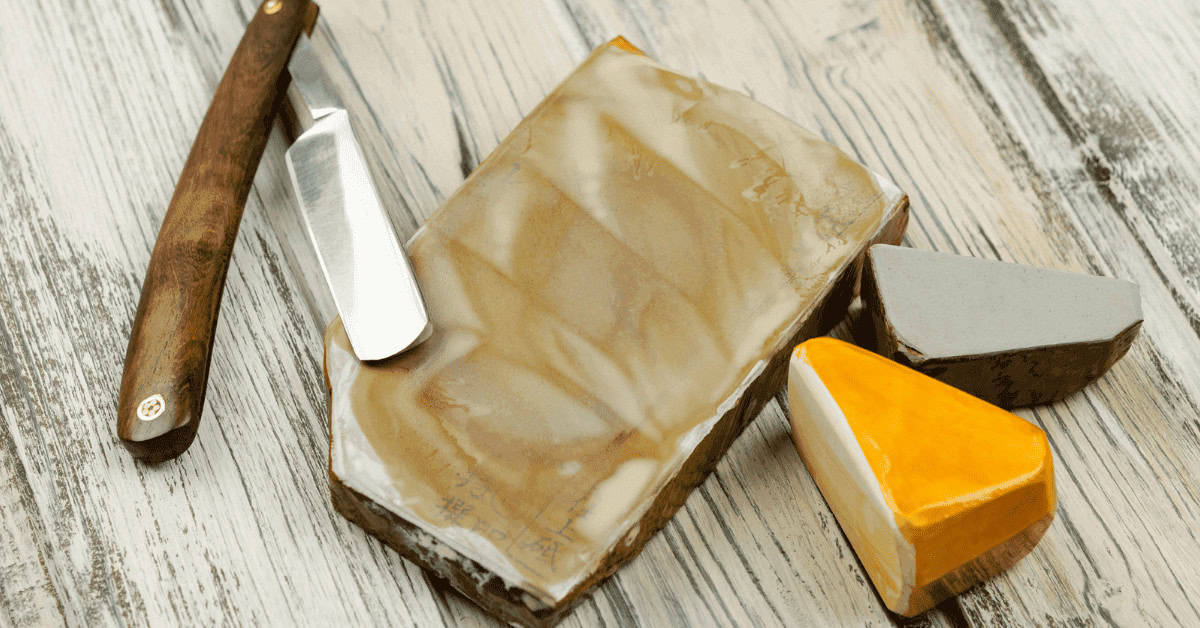 Handcrafted soap bars with a rustic wooden soap cutter on a distressed wooden surface. The soap showcases natural, marbled swirls in beige, gray, and vibrant orange tones, perfect for skincare routines.