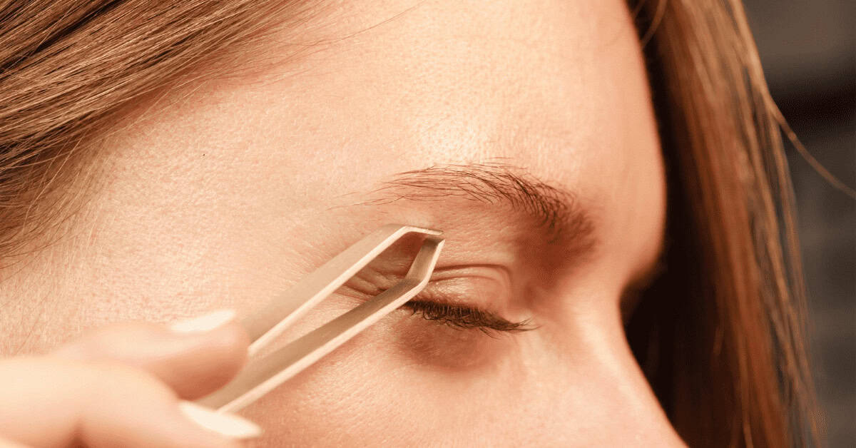 Grooming eyebrow with tweezer close-up, highlighting detailed eyebrow shaping and grooming for a polished eye makeup look.