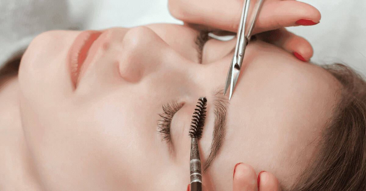 Close-up of a woman receiving eyelash extension application, with professional tools used to enhance eyelashes for a glamorous look.