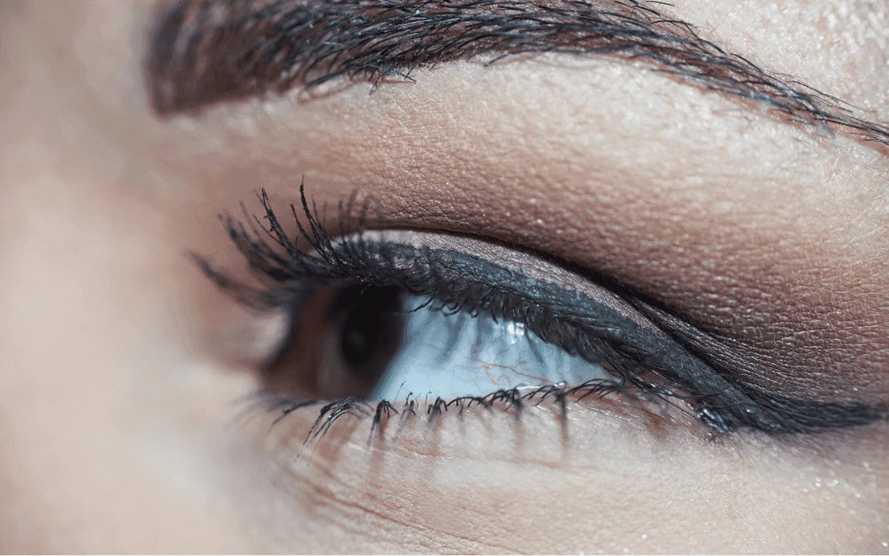 Soft focus close-up of a woman's eye showcasing flawless makeup with long, voluminous eyelashes, precise black eyeliner, and neutral eyeshadow shades, highlighting elegant eye makeup and mascara.