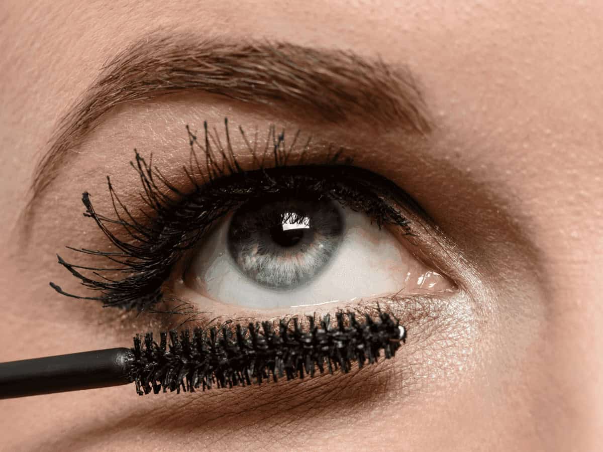 Vibrant blue eye with long, thick black eyelashes being coated by mascara, showcasing bold eye makeup and detailed eye makeup techniques.