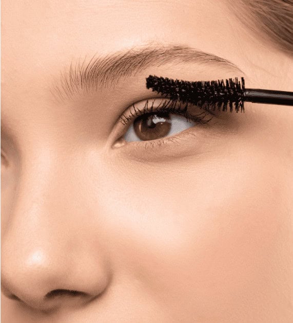 Luxurious black mascara being applied to a woman's upper eyelashes, enhancing eye makeup and creating a dramatic, full lash look.